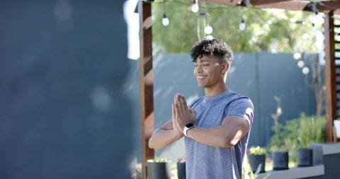 African american man smiling practicing mindfulness on sunlit backyard patio under pergola