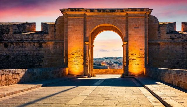 Golden limestone archway at dusk framing distant city spire with dramatic sunset glow