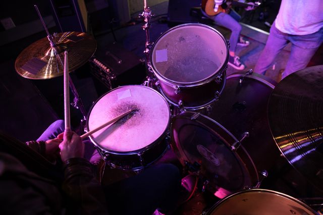 Overhead view of male drummer playing drums with his bandmates and band equipment on stage at a music venue during concert. Entertainment fun music.