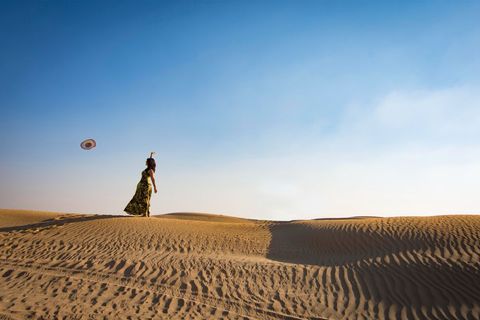 Woman Catapulting Hat in Sunlit Desert Landscape