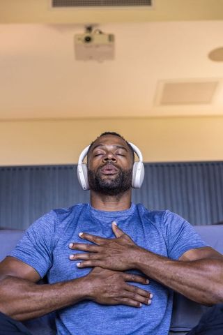 African american man listening with headphones, practicing deep breathing, relaxing at home