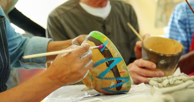 Hands of diverse individuals are engaged in painting and crafting pottery, with copy space. Artistic expression is captured as they focus on decorating ceramic pieces with vibrant colors.