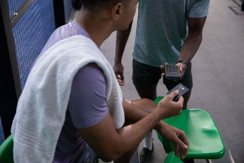 Diverse male friends using contactless card and mobile scanner in gym locker room