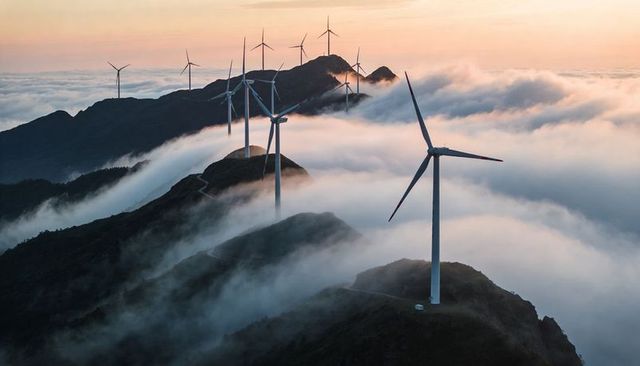 Wind turbine ridge at sunrise with fog-filled valleys and mountain cloudscape