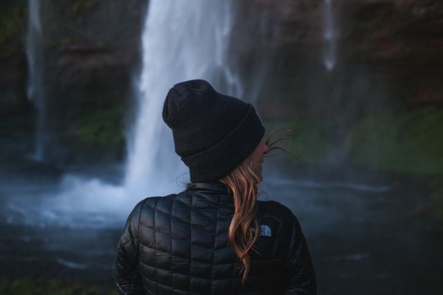 Blonde Haired Woman in Black Bubble Jacket and Black Knit Hat Beside Waterfall - Download Free Stock Photos Pikwizard.com