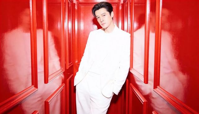 Male model wearing white suit leaning in glossy red corridor high-fashion portrait