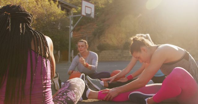 Depicts group of women stretching on an outdoor basketball court. Sunny day creates a warm and motivating atmosphere. Ideal for use in fitness, sports, outdoor activity promotions, health and wellness campaigns, and community event advertisements.