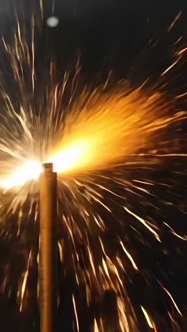 Vertical video showing metal post ejecting dramatic golden sparks and embers at night