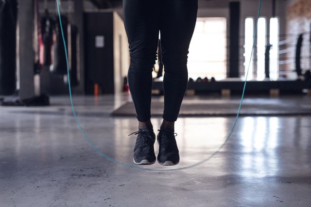 This image shows the lower body of a young female boxer jumping rope in a gym. Ideal for use in fitness blogs, sports training guides, gym advertisements, and health and wellness articles. It highlights physical activity, strength training, and cardio exercise.