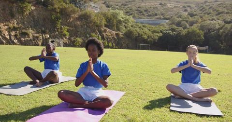 Diverse children practicing meditation outdoor in sunny field