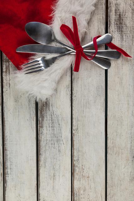Picture of cutlery tied together with a red ribbon placed on a rustic wooden board, bringing a festive and cozy touch. Ideal for holiday dining images, Christmas table settings, dining decorations, or seasonal restaurant promotions.