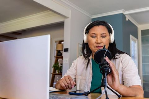 Senior woman podcasting from home studio wearing headphones and adjusting microphone