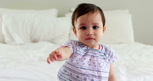 Cute baby girl sitting on bed in bedroom
