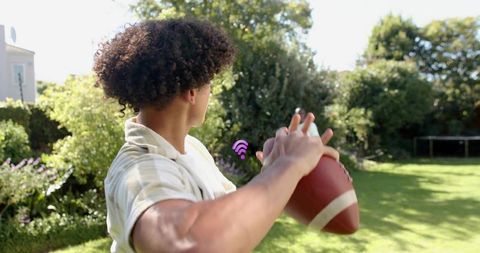 Young man preparing to throw football in sunny backyard with wi fi signal overlay