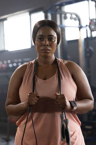 Focused african american woman standing in gym gripping jump rope wearing smartwatch
