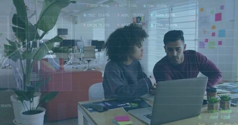 Coworkers reviewing laptop and brainstorming in modern open-plan office with sticky notes