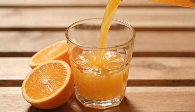 Pouring fresh orange juice into glass on rustic wooden slats with halved oranges, closeup