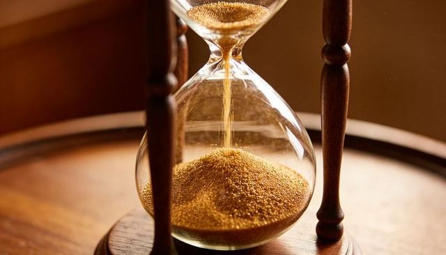 Golden hourglass flowing gold sand on turned wooden stand evoking time and patience