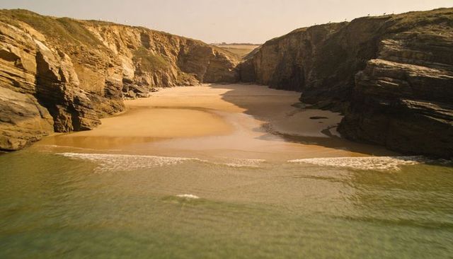 Golden cliffs framing quiet sandy cove with tidal channel and warm late afternoon light
