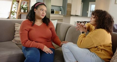 Two women talking and offering emotional support on couch in cozy modern living room