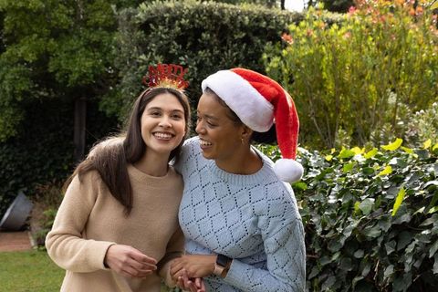 Multicultural friends laughing in backyard wearing santa hat and merry headband