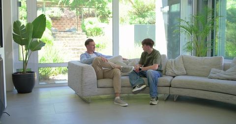 Two men having casual conversation on modern light gray sectional in sunlit living room