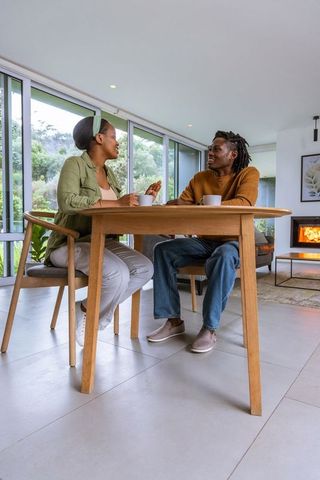 African american couple conversing over coffee at modern dining table near fireplace, cozy