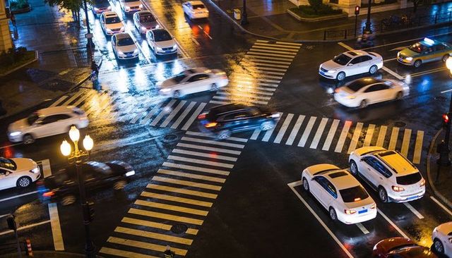 Nighttime urban intersection reflecting wet streetlights with moving cars and zebra crossings