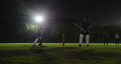 Batsman facing bowler delivering under floodlights during intense night cricket match