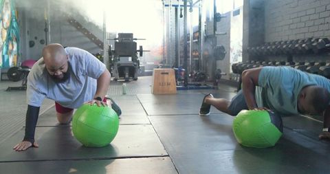 Partners performing medicine ball plank in industrial gym for core strength and balance