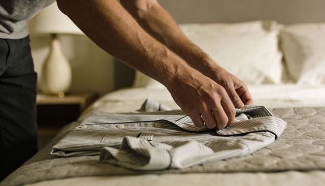 Man folding striped shirt on quilted bedspread preparing outfit for next day