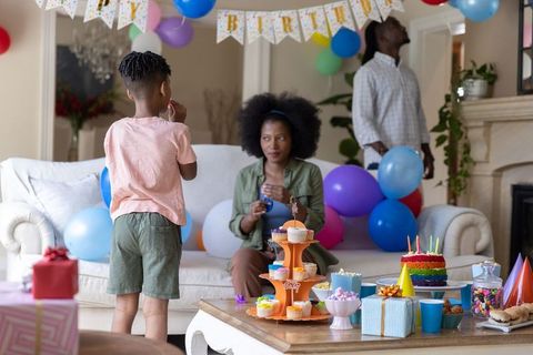 African american family celebrating child birthday at home with balloons, cake and gifts