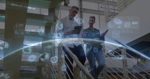 Business colleagues descending atrium stairs using tablets with holographic data interface