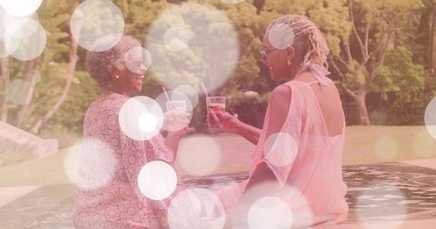Two mature women toasting by poolside, relaxing with iced drinks and sharing laughter outdoors