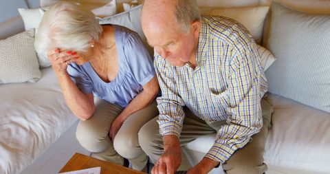 Senior Couple Anxiously Reviewing Household Bills on Couch