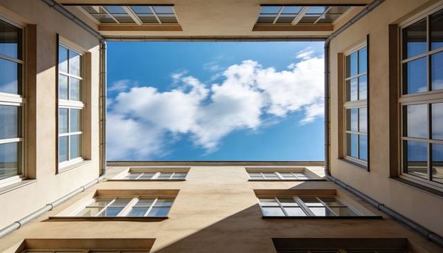 Looking up through courtyard lightwell framing blue sky and white-trim windows