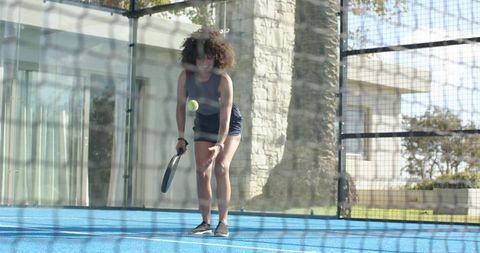 Padel player dropping ball and holding racket on blue court with net reflections
