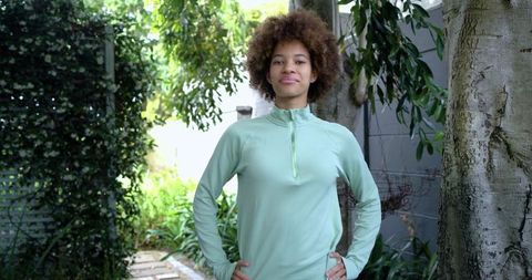 Young woman standing confidently in backyard garden wearing green athletic zip top