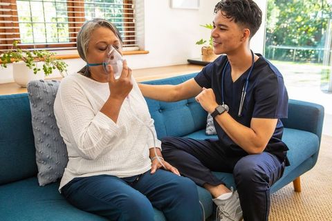 Senior woman with oxygen mask comforted by caregiver in home setting