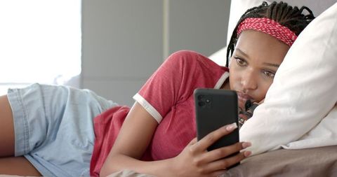 Young Woman Relaxing in Bed Browsing Smartphone