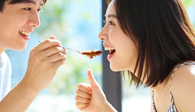 Sunlit couple sharing spoonful of dessert during joyful summer brunch moment
