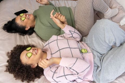 Diverse friends relaxing on bed with cucumber eye masks, cozy sweaters and loungewear