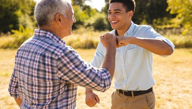 Intergenerational men exchanging fist bump in sunlit meadow expressing connection and joy