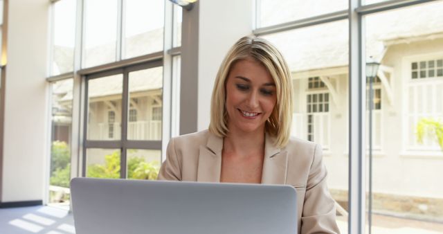 Smiling Businesswoman Working on Laptop in Modern Office with Large Windows - Download Free Stock Images Pikwizard.com