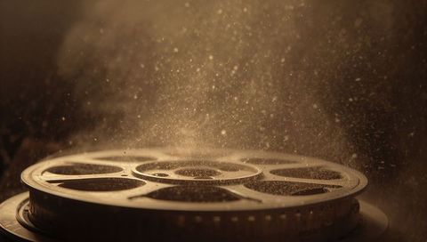 Glowing vintage film reel resting under floating dust particles with cinematic sepia bokeh