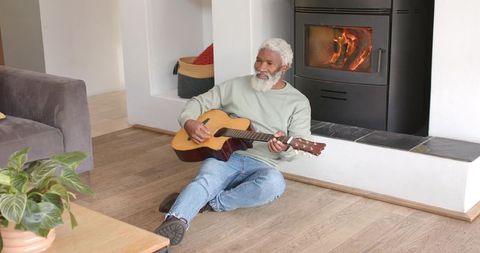 Elderly Man Playing Acoustic Guitar by Fireplace in Cozy Living Room