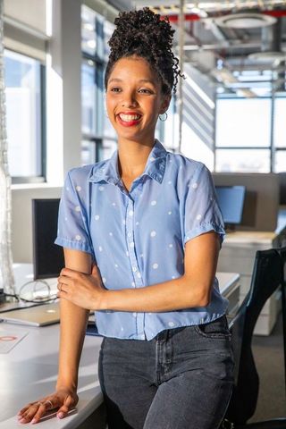 Smiling african american professional leaning on desk in modern open-plan office