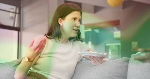 Woman gesturing while holding plate on couch in casual conversation in modern living room