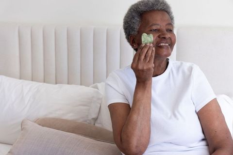Senior african american woman using heart jade gua sha for facial massage and self-care