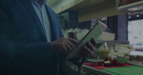 Manager tapping tablet on restaurant kitchen counter wearing blue suit, managing orders